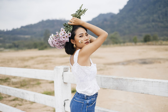 年轻性感的亚洲女人穿着白衬衫，头上举着花束，回头看着镜头。