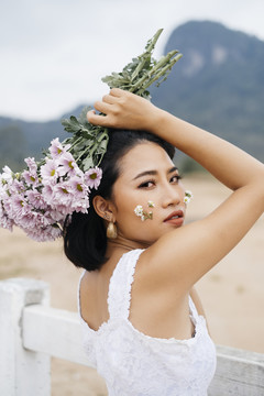 年轻性感的亚洲女人穿着白衬衫，头上举着花束，回头看着镜头。