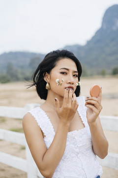 一位亚洲妇女靠着白色的篱笆在脸颊上放花化妆。