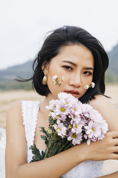 一个年轻性感的亚洲女人的特写镜头，穿着白衬衫，手里拿着粉白色的花。