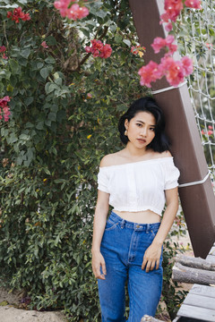 年轻性感的亚洲女人穿着白衬衫和蓝色牛仔裤站在花绿色的墙上。