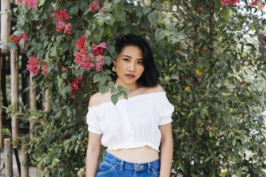 年轻性感的亚洲女人穿着白衬衫和蓝色牛仔裤站在花绿色的墙上。