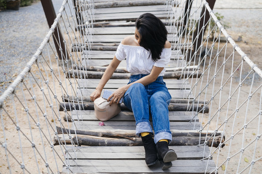性感的亚洲女人坐在木桥上，整容，从旁边的小篮子里拿起设备。