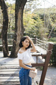 性感亚洲女人的侧视图拿着小篮子，站在木桥上享受旅行。