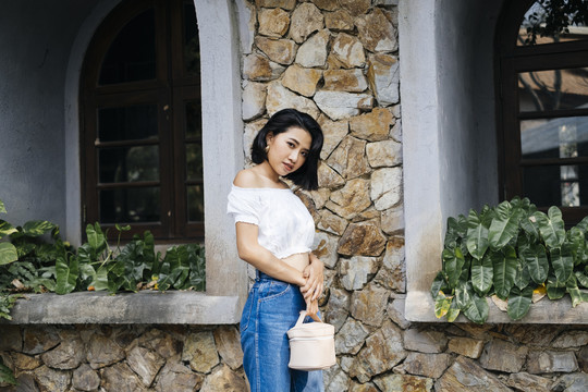 年轻性感的亚洲女人，穿着白衬衫和蓝牛仔裤站在石墙前。石墙咖啡馆的年轻旅女。