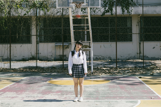 留着辫子和流苏头发的女学生站在废弃的篮球场上。