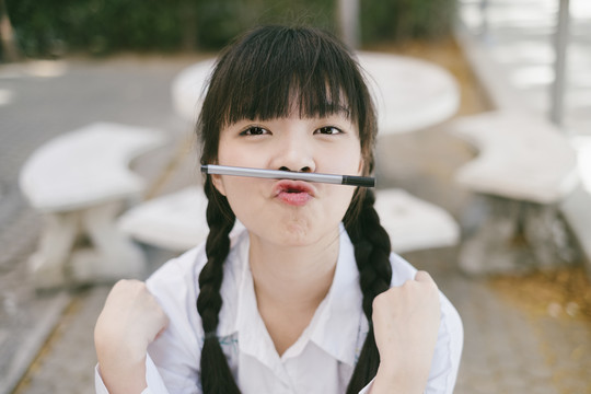 留着辫子和流苏头发的女学生做鸭脸，把笔放在嘴上。