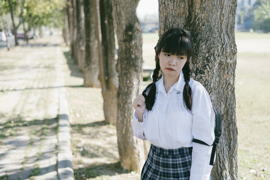 一个留着辫子和流苏头发的悲伤的女学生站在树旁。