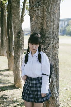 一个留着辫子和流苏头发的悲伤的女学生独自站在树旁。