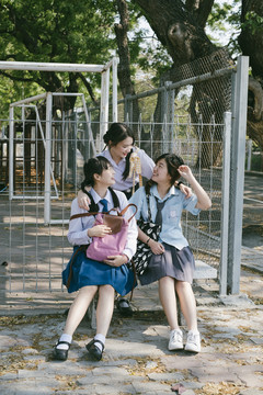 休息时间，三个穿着不同制服的漂亮亚泰学生在公园里交谈。