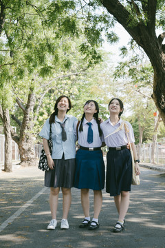三个穿着不同制服的美丽的亚泰学生在公园观光。