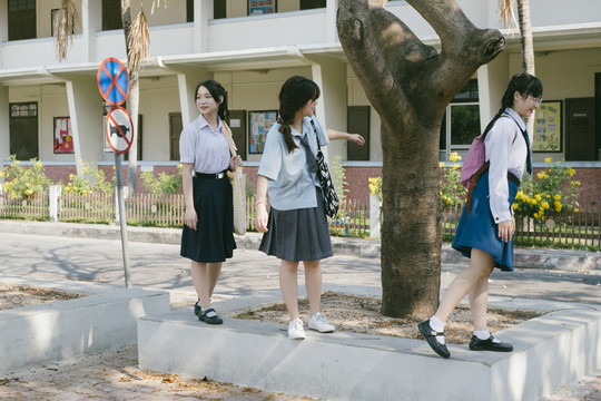 三个穿着不同制服的漂亮亚泰学生在水泥地上散步。