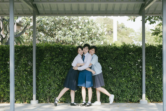 三个穿着不同制服的漂亮亚泰学生互相拥抱。