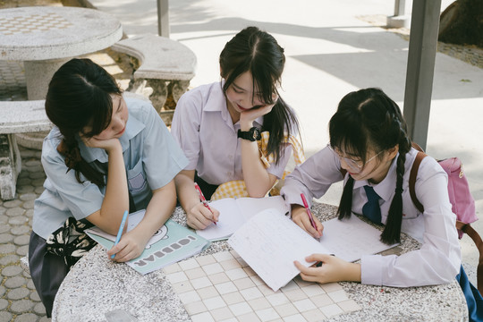 三个穿着不同制服的漂亮亚泰学生互相帮助完成作业。教作业。