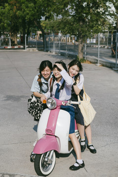 三个穿着不同制服的美丽亚泰学生在学校玩着白色粉色粉彩摩托车。