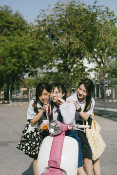 三个穿着不同制服的美丽亚泰学生在学校玩着白色粉色粉彩摩托车。