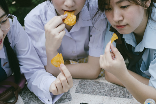 三个穿着不同制服的漂亮亚泰学生在课间休息时一起吃薯片。