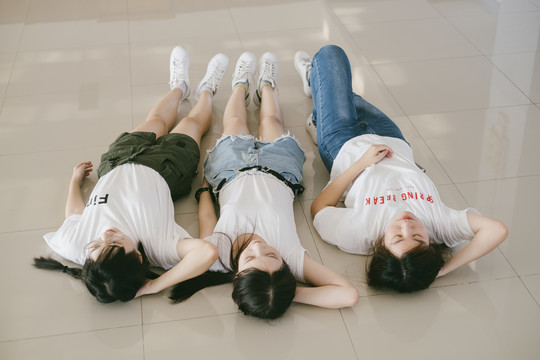 三个穿着休闲白衬衫的美丽亚泰学生躺在地板上。一起睡觉和放松。