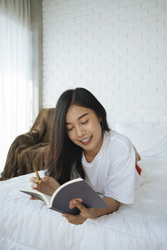 一个亚洲女孩在床上看书，脸上带着微笑。