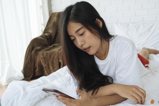 美丽的泰国年轻女子在床上玩手机。