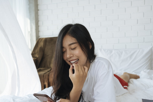 年轻的泰国女士喜欢在床上玩手机和笑。