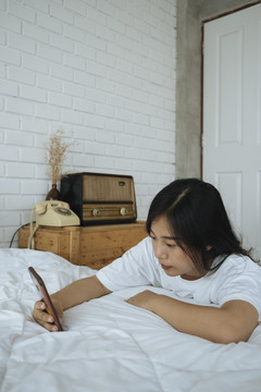 可爱的亚洲女人玩手机，和朋友聊天，在facebook上工作。白色卧室。