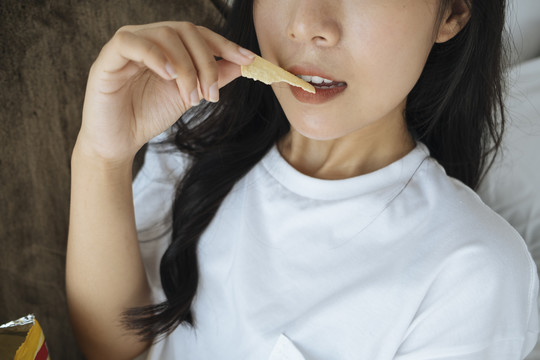 亚洲年轻女子吃薯片的特写镜头，摆出性感的姿势。