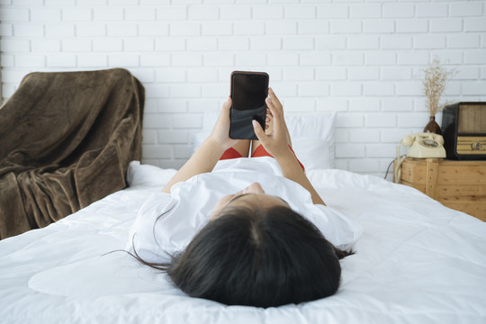 亚洲女士在床上玩手机-正面视图。