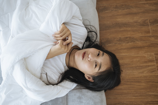 亚洲年轻女子躺在床上用白色毯子盖住身体的俯视图。快乐和微笑。