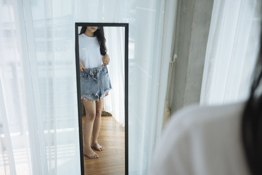 苗条的亚洲女人在镜子前试穿牛仔裤-购物概念。