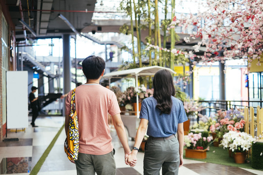一对亚泰夫妇手牵手走在购物中心。
