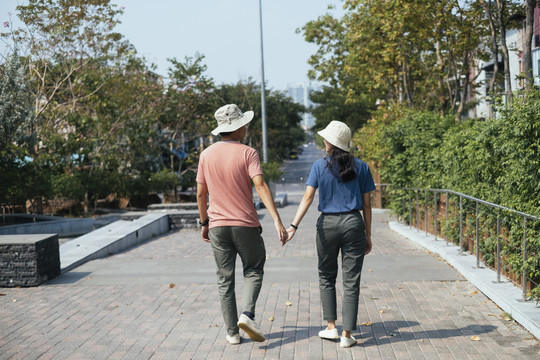 后视图-亚泰夫妇戴着帽子，手牵手一起在公园散步。