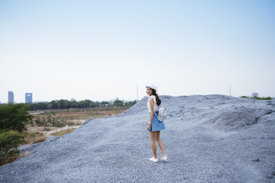 美丽的亚泰旅行家妇女戴着帽子和白色袋子站在岩石山的侧视图。刮风的日子。