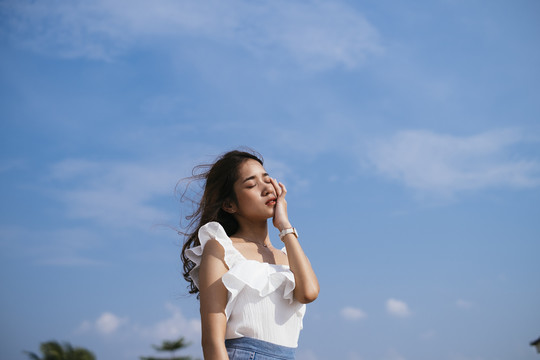 棕褐色皮肤性感美丽的亚泰旅行家女子在白色衬衫在风天在蓝天背景。