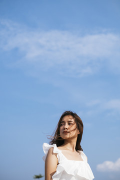 棕褐色皮肤性感美丽的亚泰旅行家女子在白色衬衫在风天在蓝天背景。