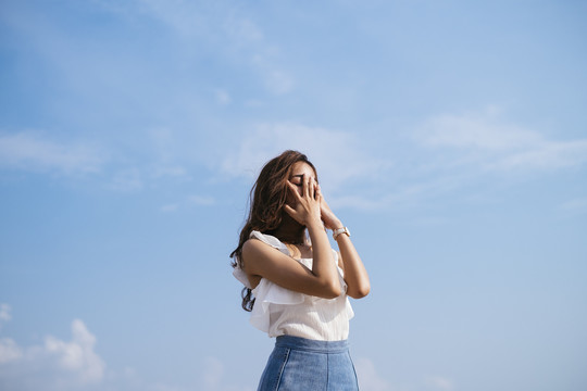 棕褐色皮肤性感美丽的亚泰旅行家女子在白色衬衫在风天在蓝天背景。