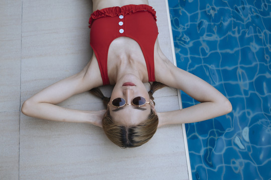 俯瞰图-身着红色比基尼的泰国美女躺在泳池边。