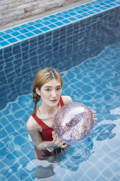 身着红色比基尼的泰国美女在游泳池里游泳，透明闪闪发光。