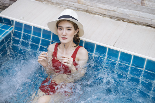 身着红色比基尼、戴着帽子和太阳镜的泰国美女在按摩浴缸游泳。