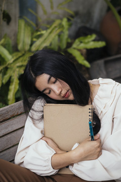 一位年轻的女记者睡在花园的长凳上，抱着一本书。书迷。