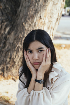泰国年轻女子黑发特写肖像。面部表情。双手抓脸颊。