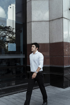 穿着白色正式衬衫的成熟亚洲商人在大楼外的街道上行走。