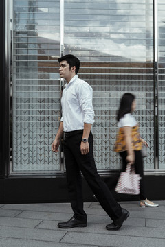 穿着白色正式衬衫的成熟亚洲商人走在人群中。