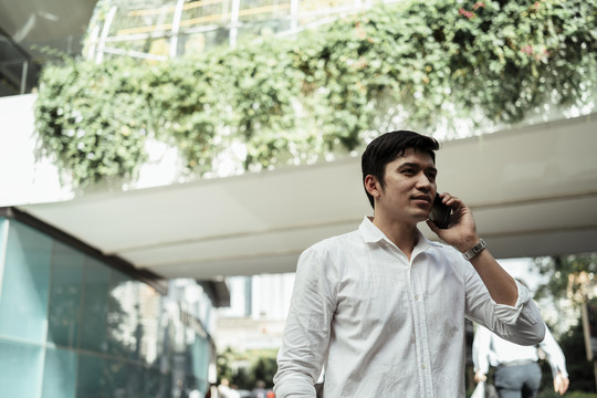 在livewall，一位穿着白色正式衬衫的成熟亚洲商人一边微笑一边打电话。