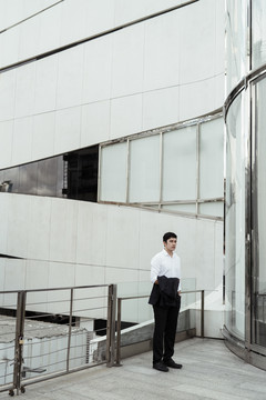 穿着白色正式衬衫的成熟亚洲商务人士在办公室外的走道上行走。