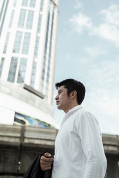 穿着白色正式衬衫的成熟亚洲商人在城市的蓝天下走在街上。