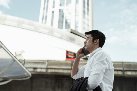 在大城市里，穿着白色正式衬衫的成熟亚洲商务人士用智能手机打电话。