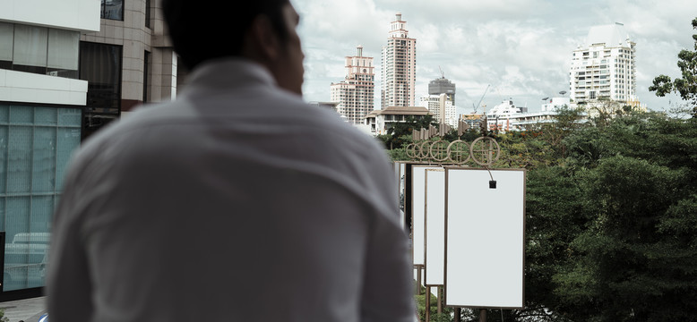 后视图-穿着白色正式衬衫的成熟亚洲商人站在阳台上看城市。