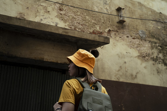 一个背着绿色背包的黄色背包女站在镇上一栋又旧又生锈的房子前。