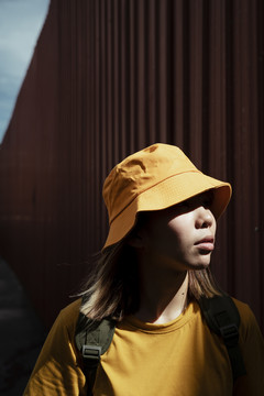 夏天，穿着黄色t恤的背包女孩沿着红色金属墙散步。